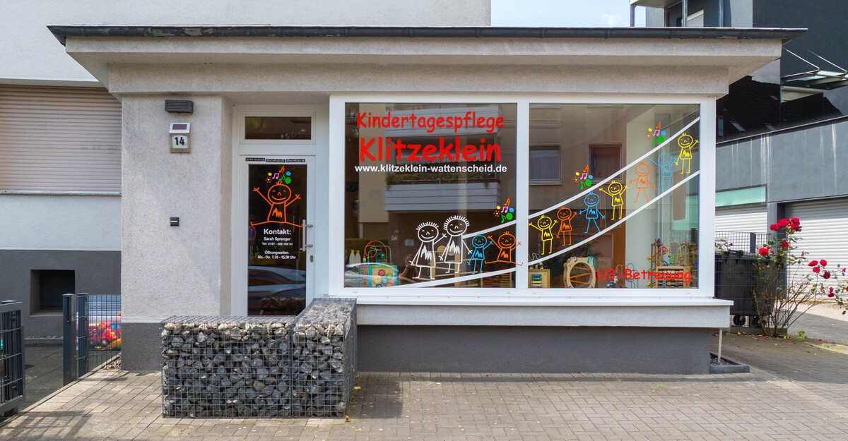 Ansicht von außen der Kindertagespflege Klitzeklein in Wattenscheid, mit einem großen Schaufenster, bunten Kinderzeichnungen und der Beschriftung 'Kindertagespflege Klitzeklein'.