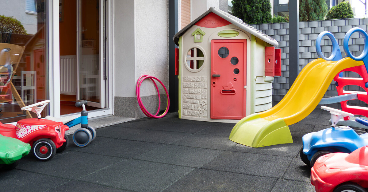Außenbereich der Kindertagespflege Klitzeklein mit Spielhaus, Rutsche, Bobby-Cars und Hula-Hoop-Reifen.